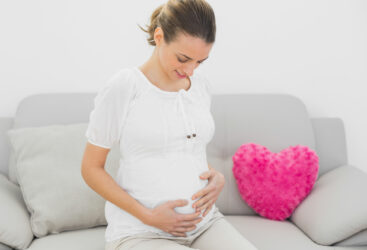 Kobieta w ciąży siedzi na kanapie i trzyma się za brzuch