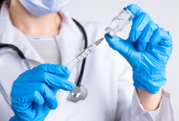 Lekarz w masce i rękawiczkach gumowych napełnia strzykawkę wbita w fiolkę